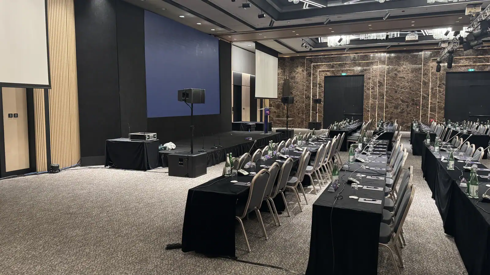 Conference microphones arranged in a large congress hall with a stage and LED screen.